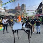 Figura 1. La mula de hierro y el pebetero encendido en el parque principal de Valdivia. Nota: los deportistas locales portan la antorcha, junto al artefacto simbólico central de los Juegos Campesinos. Al fondo, la iglesia del municipio. En términos de Bijker (1995), la mula de hierro funciona como un artefacto con flexibilidad interpretativa: homenaje a la vida campesina, espejo de identidad montañera e imagen condensadora de toda la narrativa mediática. Valdivia, Antioquia, 10 de septiembre de 2025. Fotografía del autor.